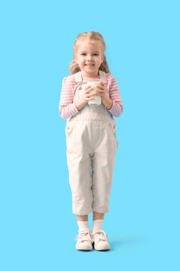 Mavi arka planda bir bardak sütü olan tatlı küçük bir kız.