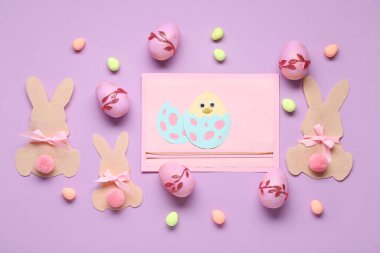 Paskalya tavşanları, boyalı yumurtalar ve eflatun kaplama tavuklu kartlar. Üst görünüm