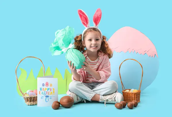 可爱的小女孩 长着小兔子耳朵 戴着复活节彩蛋 蓝色背景上装饰着纸 — 图库照片