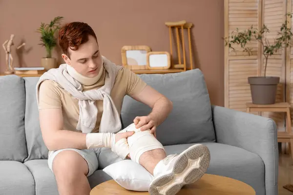 Injured young man after accident with his leg on pillow at home