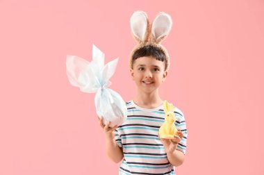 Paskalya hediyesi yumurtası ve pembe arka planda bir tavşanla tavşan kulağı takan sevimli bir çocuk.