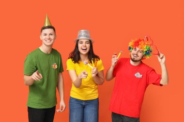 Kağıt balıklar ve ıslıklarla kılık değiştirmiş genç arkadaşlar turuncu arka plandaki izleyiciye bakıyor. 1 Nisan kutlamaları