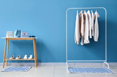 Mavi duvarın yanında şık kıyafetler, ayakkabılar ve aksesuarlarla dizilin.