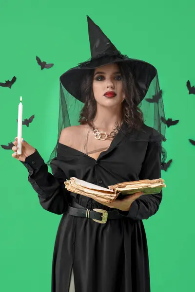 Young witch with spell book, candle and bats on green background