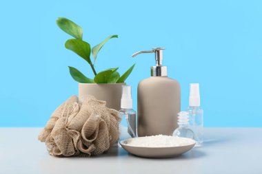 Mavi duvarın yanındaki masada deniz tuzu ve duşlu puf ile kompozisyon. Banyo aksesuarları