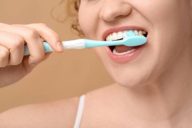 Kahverengi arka planda dişlerini fırçalayan genç ve güzel bir kadın.