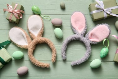 Paskalya yumurtalı tavşan kulakları ve yeşil ahşap arka planda hediye kutuları.