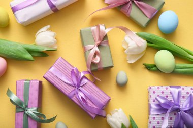 Paskalya yumurtaları hediye kutuları ve turuncu arka planda lale çiçekleri.