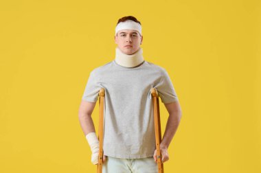 Sarı arka planda koltuk değnekleriyle kazadan sonra yaralanan genç adam.