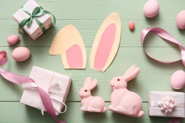 Paskalya yumurtaları ve yeşil ahşap arka planda hediye kutuları olan kağıt tavşan kulakları.
