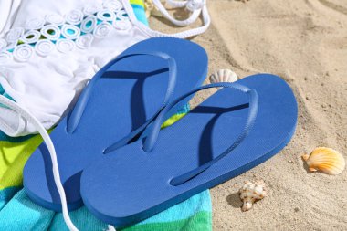 Bir çift mavi parmak arası terlik ve kumlu arka planda mayo.