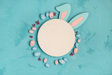 Paskalya yumurtaları, çiçekler ve turkuaz grunge arka planında kağıt tavşan kulakları olan boş bir kart.