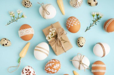 Paskalya yumurtaları, hediye, küçük çiçekler ve mavi arka planda oyuncak havuçlar.