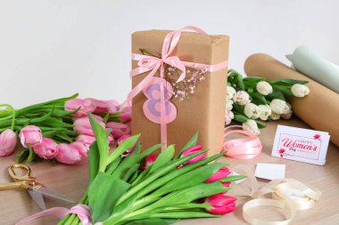 Uluslararası Kadınlar Günü için ahşap masadaki hediye kutusu, paketleme malzemeleri ve güzel lale çiçekleri.