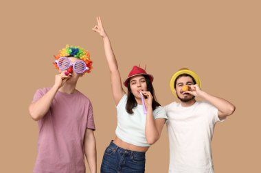 Kahverengi arka planda parti düdükleriyle kılık değiştirmiş genç arkadaşlar. 1 Nisan kutlamaları