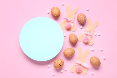 Paskalya yumurtaları, kağıt tavşanlar ve pembe arka planda boş bir kart. Üst görünüm