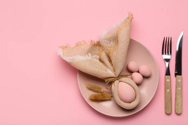 Pembe arka planda boyanmış Paskalya yumurtaları, peçete ve çatal bıçak seti ile güzel bir masa.