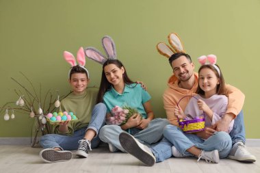 Tavşan kulaklı mutlu aile. Paskalya hediyeleri yeşil duvarın yanında oturuyor.