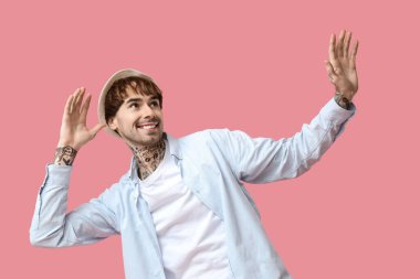 Pembe arka planda dans eden dövmeli genç adam.