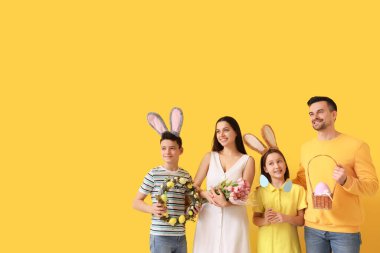 Sarı arka planda Paskalya hediyeleri olan tavşan kulaklı mutlu bir aile.