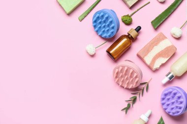 Saç derisi masaj aletleri, şampuan barları, kozmetik ürünleri şişeleri ve pembe arka planda çiçekler.
