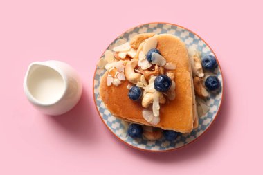 Kalp şeklinde lezzetli gözlemeler, pembe arka planda yabanmersini ve süt. Sevgililer Günü kutlaması