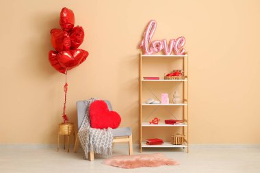 Gri koltuk, kalp şeklinde balonlar ve bej duvarın yanında Sevgililer Günü kutlamaları için dekorasyonlu kitaplık.