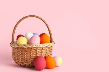Pembe arka planda boyanmış Paskalya yumurtaları olan hasır sepet.