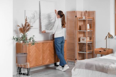 Yatak odasındaki ışık duvarına 3 boyutlu resim asan genç bir kadın.