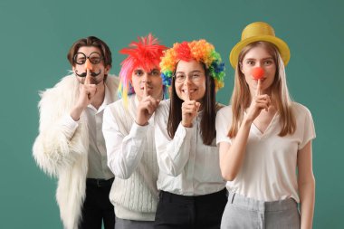 Tuhaf kılık değiştirmiş iş arkadaşları yeşil arka planda sessizlik jesti gösteriyor. 1 Nisan Kutlaması