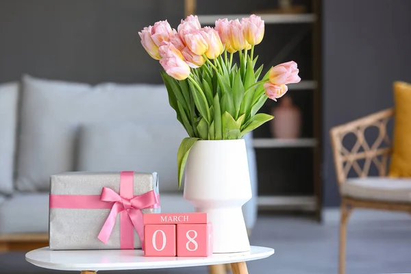 Calendar with date of International Women\'s Day, tulips and gift box on table in living room, closeup