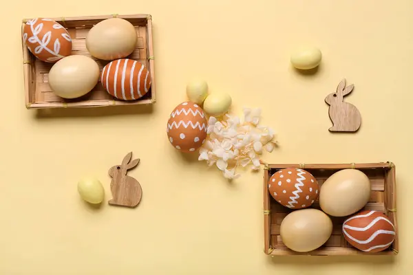Wicker boxes with different painted Easter eggs on beige background