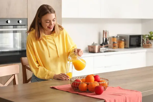 Young woman pouring orange juice into glass in kitchen