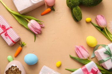 Paskalya yumurtasından yapılmış bir çerçeve hediye kutuları ve bej arka planda lale çiçekleri.