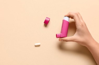 Astım spreyli çocuk eli ve bej arka planda hap.