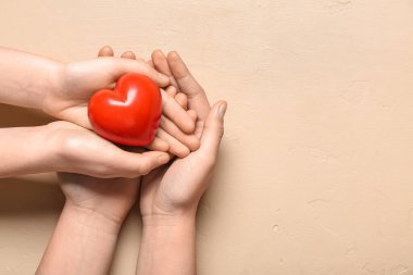 Bej arka planda kırmızı kalp tutan kadın ve çocuğun elleri