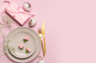 Şirin Paskalya sofrası, pembe arka planda hediyeler, çiçekler ve yumurtalar.