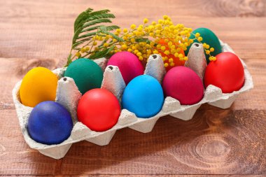 Kağıt tutacağı, boyanmış Paskalya yumurtaları ve ahşap arka planda mimoza çiçekleri.