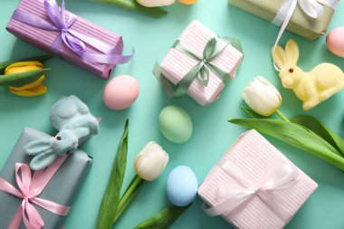 Paskalya yumurtaları, lale çiçekleri hediye kutuları ve turkuaz arka planda tavşanlar.