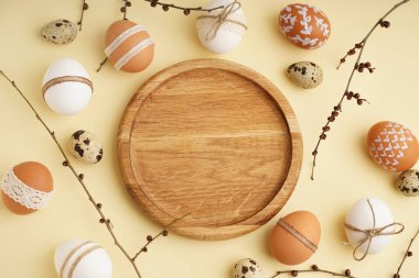 Ahşap plakalı kompozisyon, bej arka planda Paskalya yumurtası ve dalları