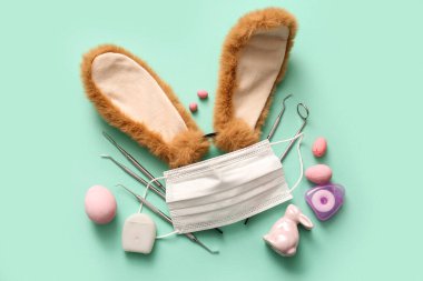 Paskalya yumurtalı tavşan kulakları, tıbbi maske ve turkuaz arka planda diş aletleri.