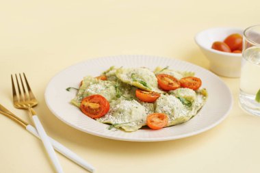 Bir tabak lezzetli ravioli, domates ve peynirli sarı arka plan.