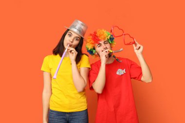 Turuncu arka planda ıslık çalan komik görünümlü genç arkadaşlar. 1 Nisan kutlamaları