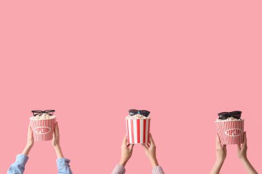 Patlamış mısır kovaları ve pembe arka planda 3 boyutlu gözlüklü eller.