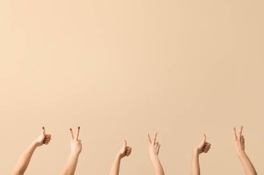 Bej arka planda barış ve baş parmak hareketlerini gösteren kadın elleri