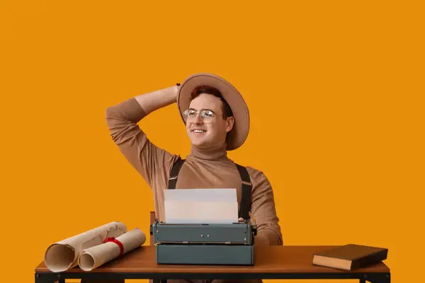 Young man with vintage typewriter at table on yellow background