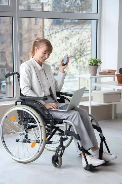 Young businesswoman in wheelchair with laptop and mobile phone at office