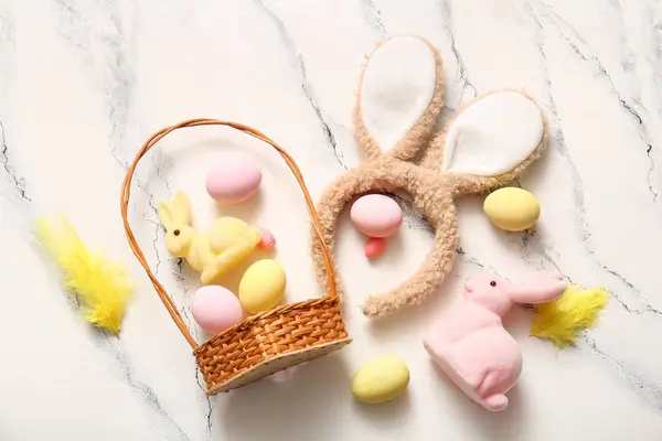 Paskalya yumurtaları ve beyaz mermer arka planda hasır sepetli tavşan kulakları.