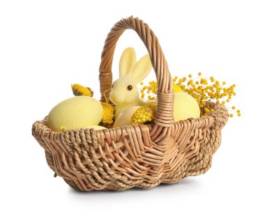 Beyaz arka planda boyanmış Paskalya yumurtaları, oyuncak tavşanlar ve çiçeklerle dolu bir sepet.