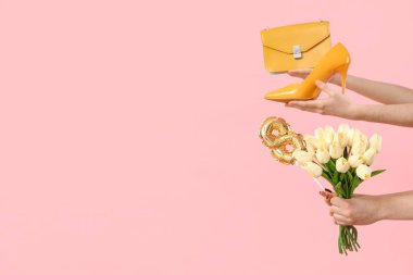 Bir buket lale, yüksek topuklu ayakkabı ve pembe arka planda el çantası olan kadın elleri. Uluslararası Kadınlar Günü için Alışveriş
